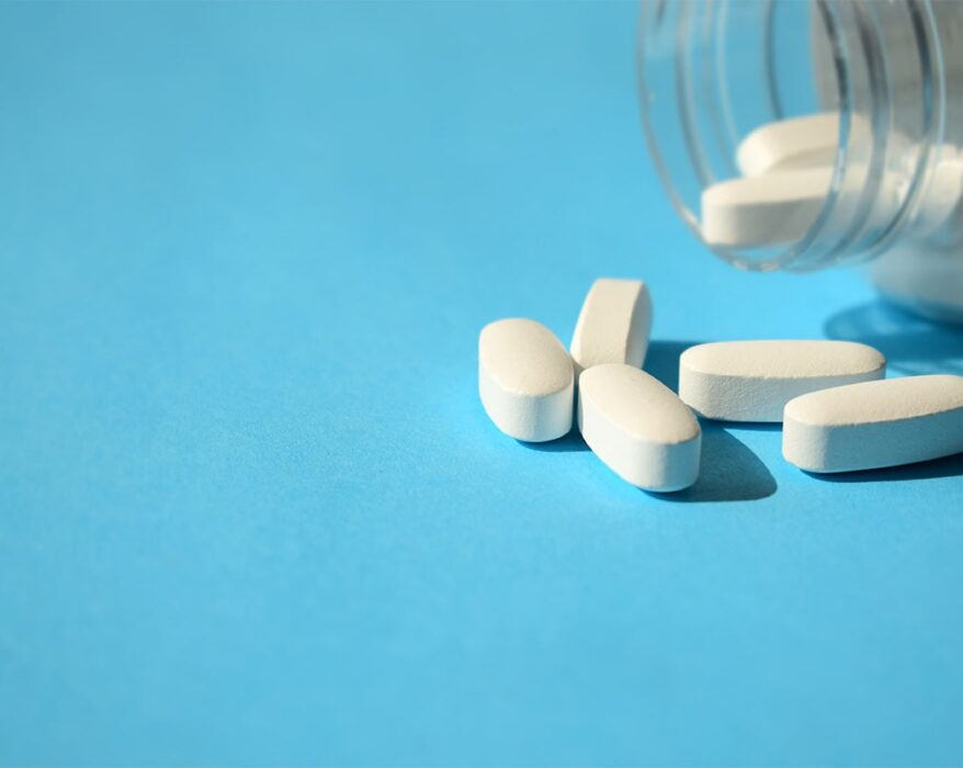 Frasco de pastillas blancas sobre fondo celeste