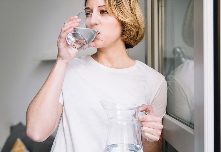 Mujer tomando agua cerca de una ventana