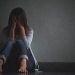 Mujer deprimida sentada en el piso y agarrando su cabeza