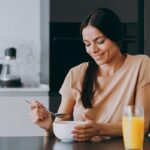 Mujer sonriendo y desayunando en su cocina